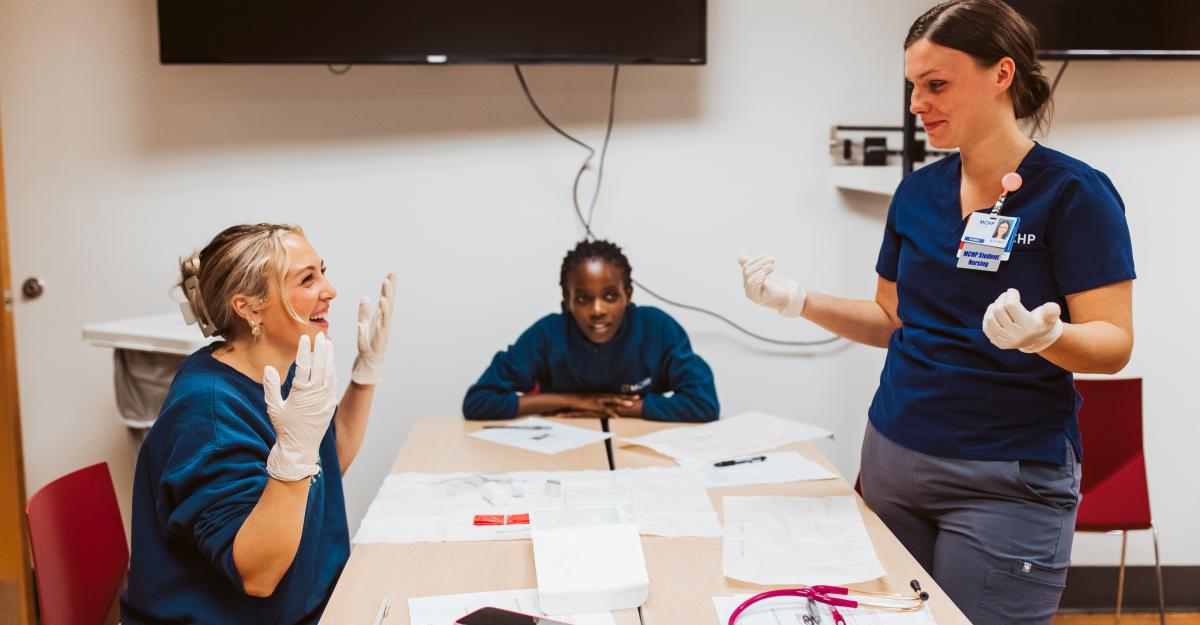 Three nursing students sit at a table together, laughing. 